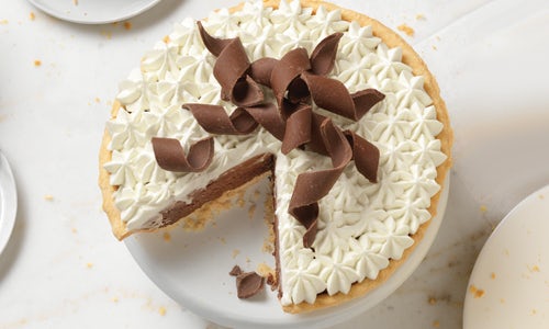 A French Silk pie topped with whipped cream and chocolate shaving, a large slice has been cut out