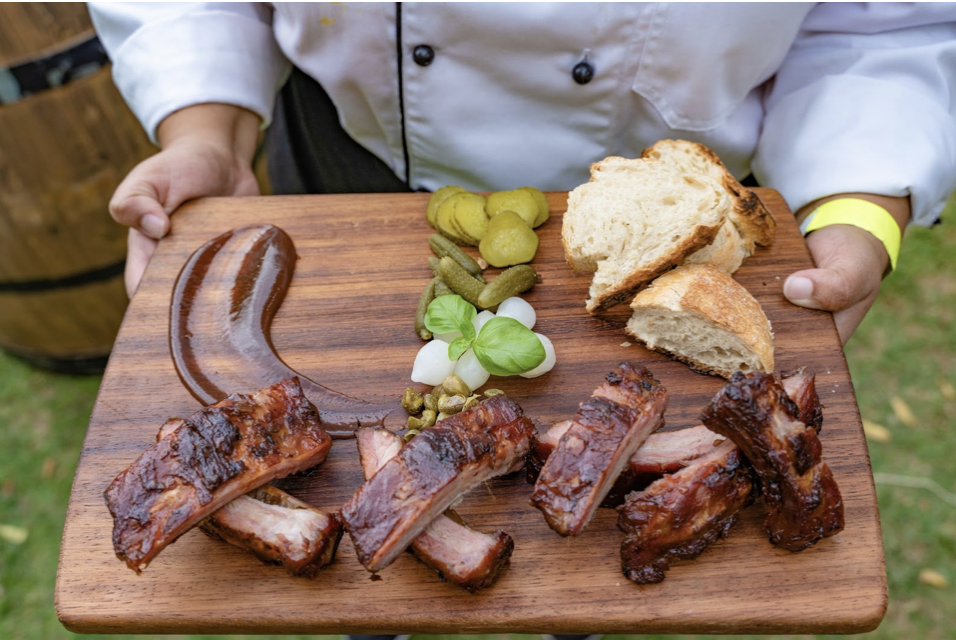 Famous Dave's BBQ Platter on a black tray with roasted chicken, chicken wings, breaded chicken, ribs, pickles, shoestring pickles, pickled onions, celery and carrot sticks, and various dipping sauces