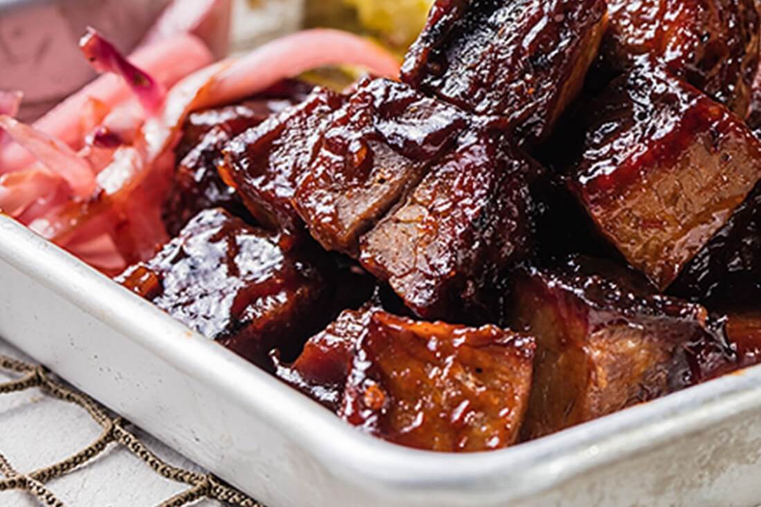 Famous Dave's Southside Rib Tips smothered in BBQ sauce with pickled onions on the side