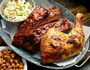 Famous Dave's ribs and chicken thigh on a metal platter with a ramekin of coleslaw