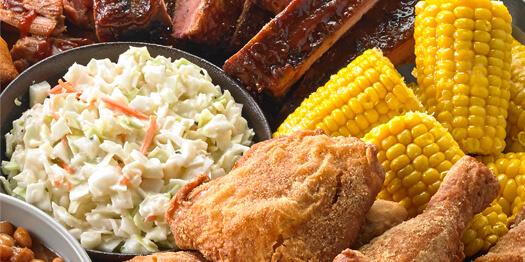 Image of Iris’ Down Home Fried Chicken, accompanied by a bowl of cole slaw, corn on the cob, some ribs and shredded meat smothered in BBQ sauce
